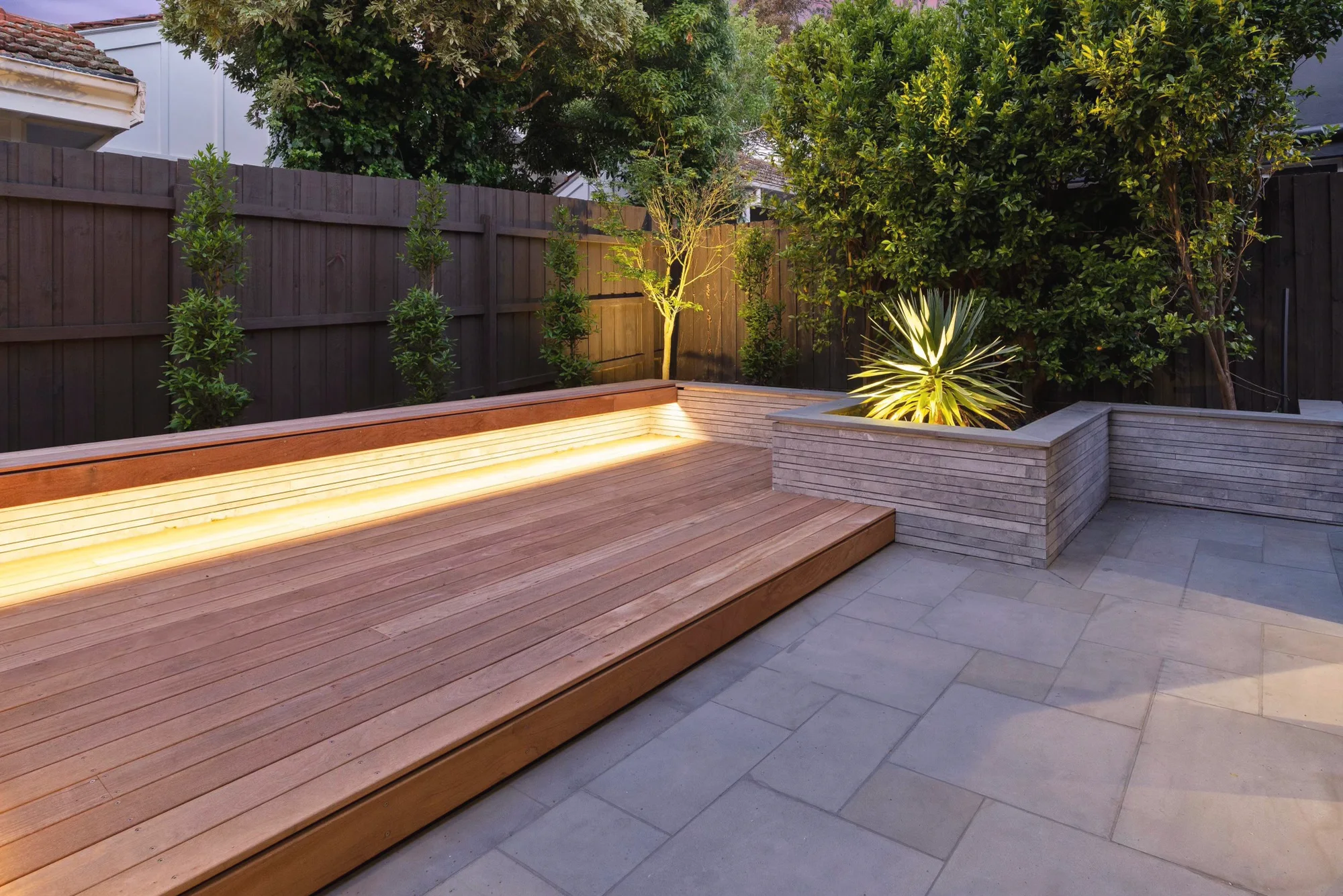 Hardwood deck with an LED strip under the bench and a stone-clad planter at dusk