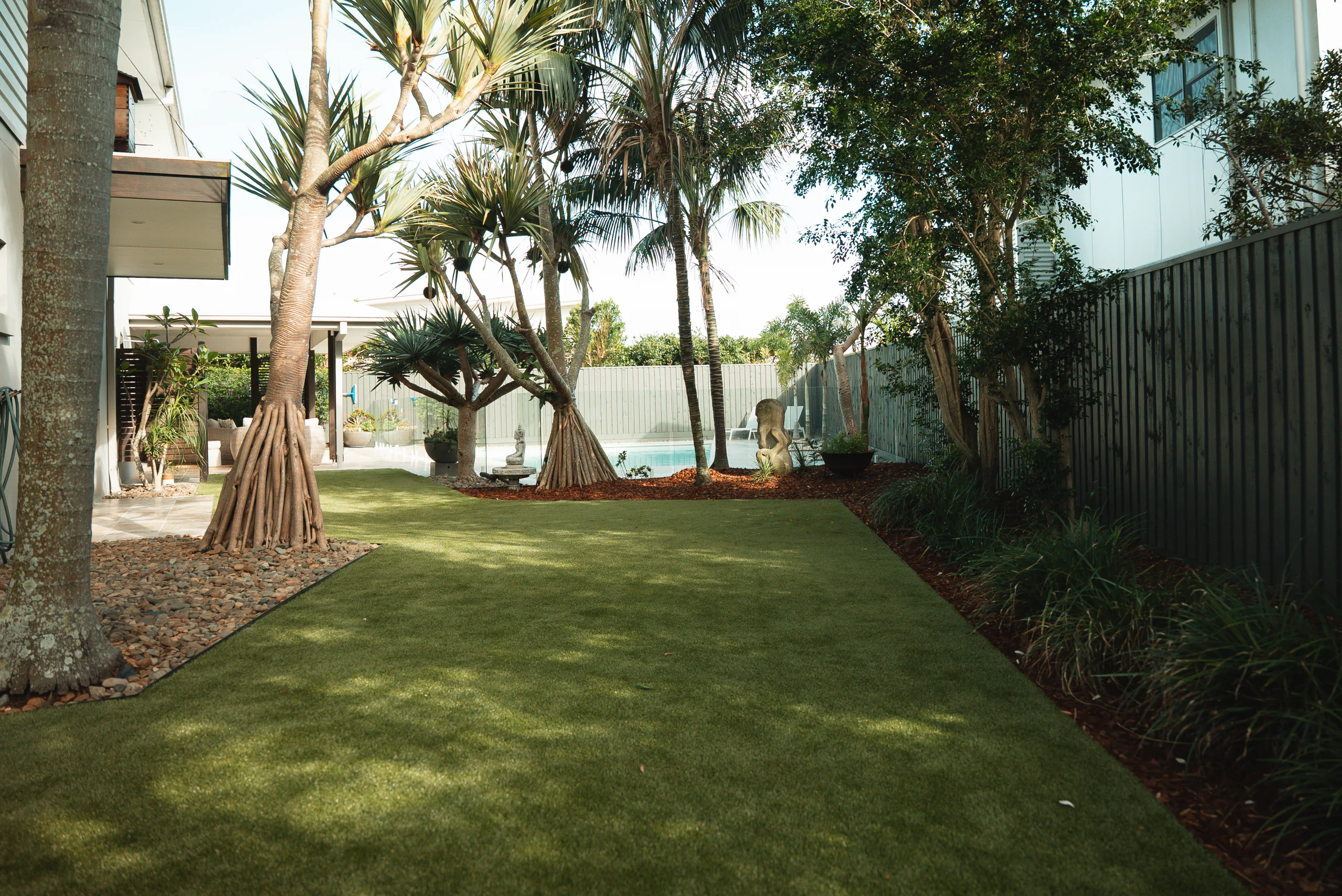 Lawn and garden beds under pandanus palms, leading to a fenced pool