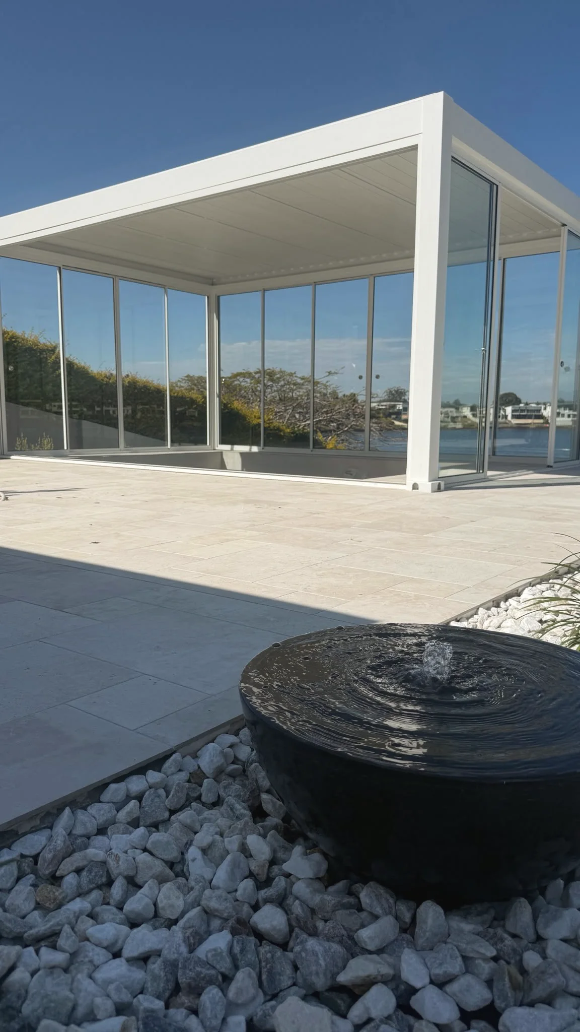 Black bowl water feature in white pebbles on a limestone terrace beside the water