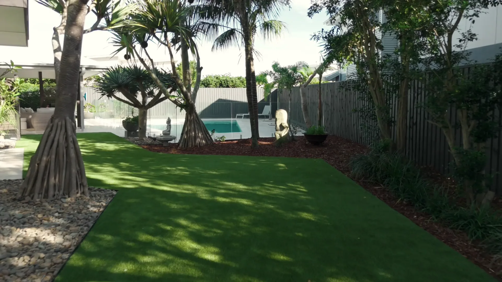 A finished Gold Coast pool garden: travertine surround, palms, lawn and pebble beds